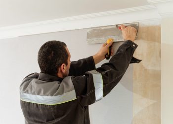 Man is cutting wallpaper. Maintenance repair works renovation in the flat. Apartment renovation and restoration idea indoors.