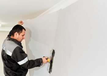 Worker attaching wallpaper. Man is putting up wallpapers on the wall. Home renovation concept