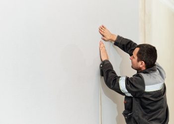 Worker pasting wallpapers. Glueing wallpapers at home. Man, worker is putting up wallpapers on the wall. Home renovation concept
